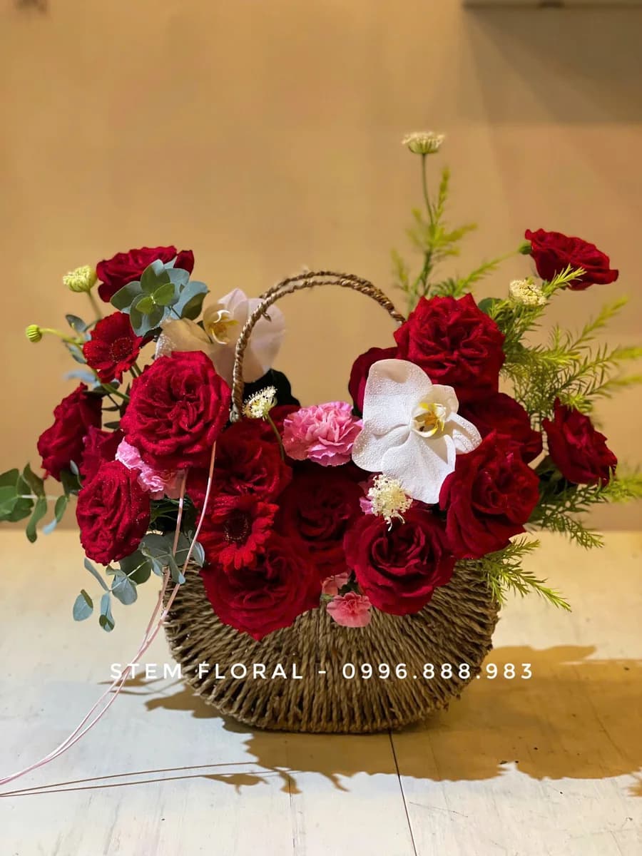 Giỏ hồng đỏ — Hoa đỏ đậm được xếp thành nhiều tầng quanh quai giỏ mây, xen cánh lan trắng và lá xanh