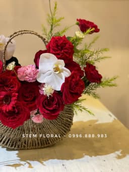 Góc 3 của Giỏ hồng đỏ — Hoa đỏ đậm được xếp thành nhiều tầng quanh quai giỏ mây, xen cánh lan trắng và lá xanh