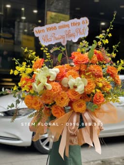 Góc 2 của Nắng ấm ngày vui — Hoa cam và vàng phối cùng các bông trắng kem, trải rộng trong thiết kế có nơ màu sáng